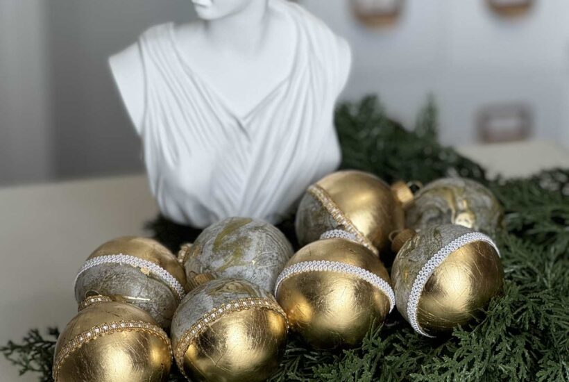 DIY Gold leaf ornaments on a bed of evergreens with statue behind.