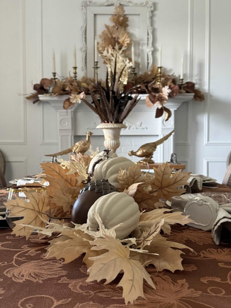 Neutral pumpkins, acorns, and leaves in the center of a Thanksgiving tablescape. 