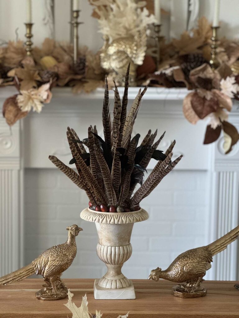 Two gold pheasant statues on either side of an urn filled with pheasant feathers. 