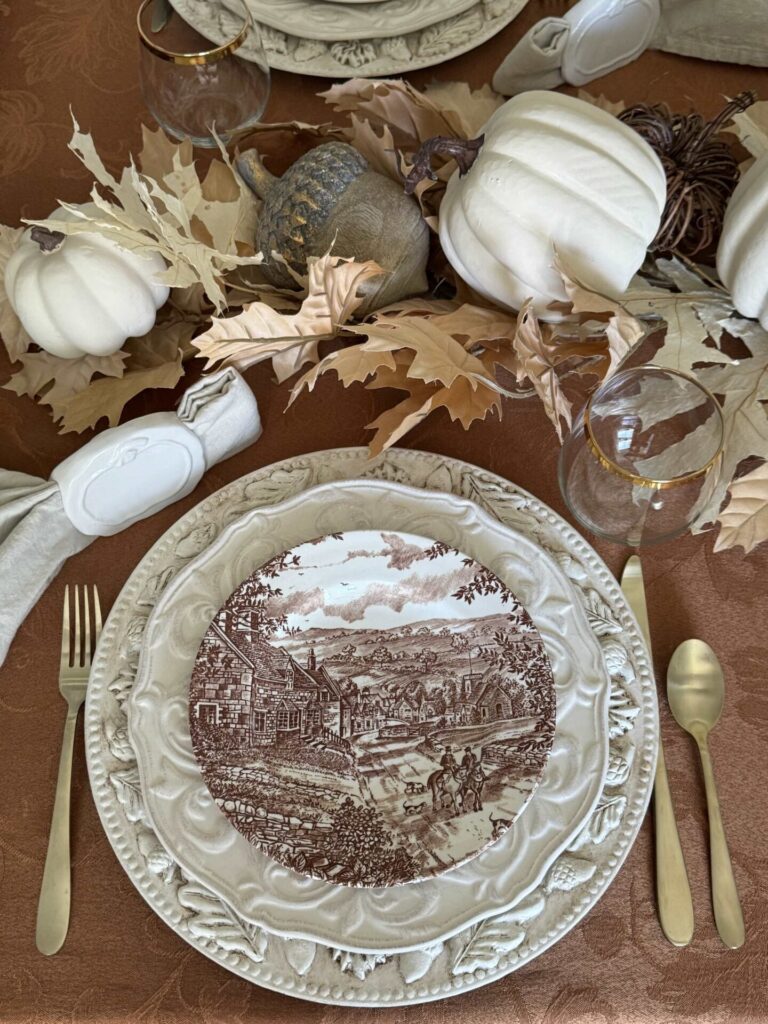 A Thanksgiving tablesetting with a charger, cream dinner plate, and brown transferware salad plate. 