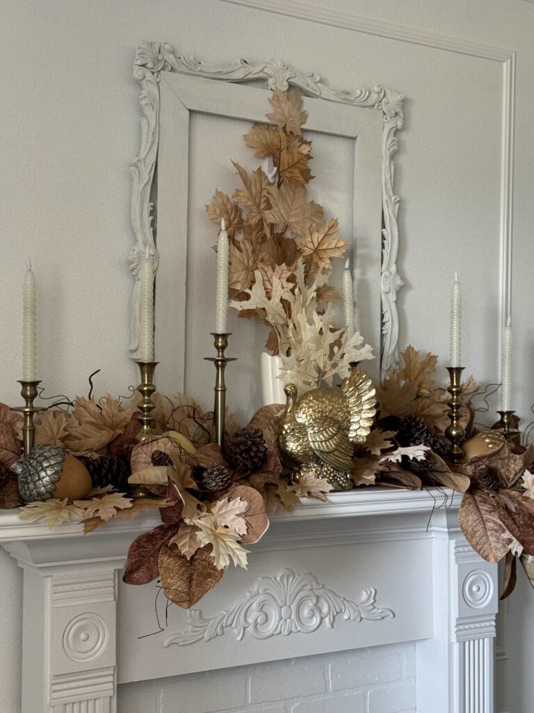 A white mantel decorated with brown and tan leaves and a gold turkey. 