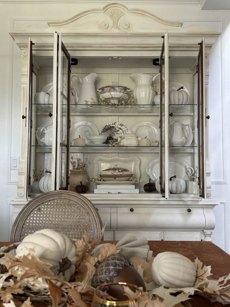 A china cabinet with white ironstone, brown transferware, and pumpkins.  