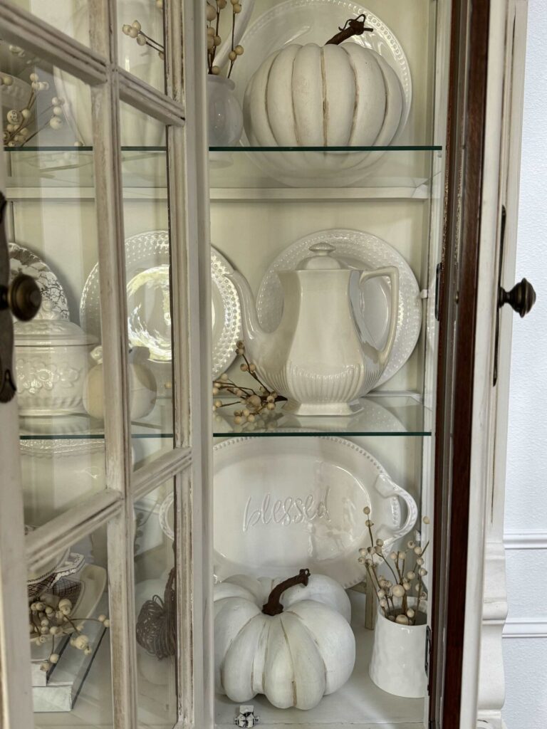 White dishes and pumpkins in a china cabinet. 