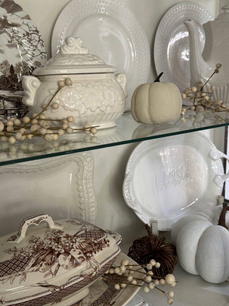 Small white tureen and pumpkins in a china cabinet. 