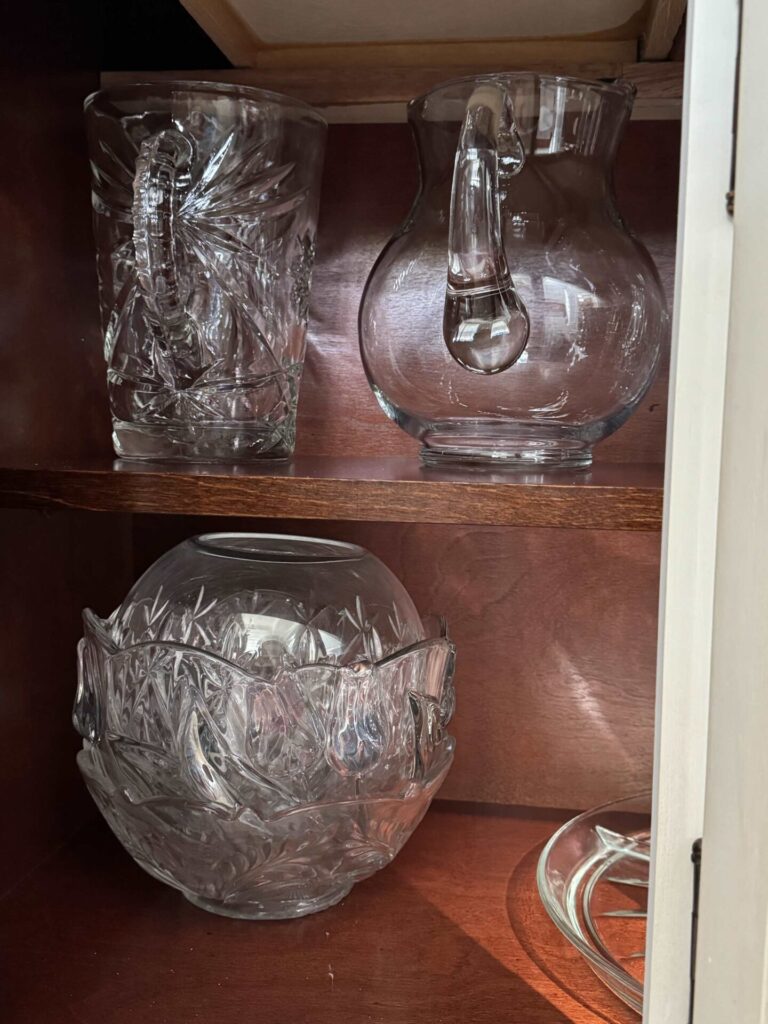 Glass pitchers and bowls organized in a china cabinet.