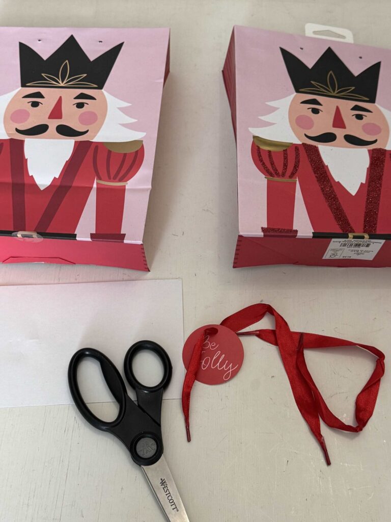 Step two to make DIY Christmas wall decor is to cut a gift bag in half with scissors and remove the ribbon handles and tag. 