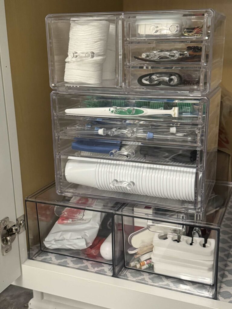 Clear plastic stacking drawers organized under a bathroom sink. 