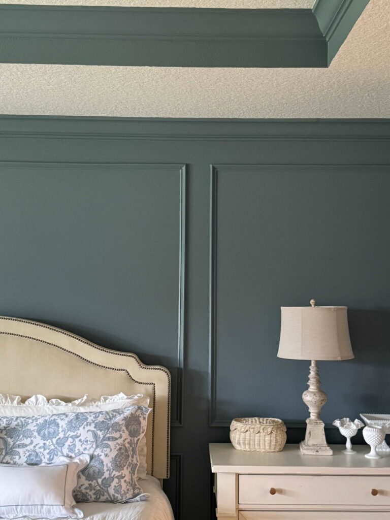 A bedroom with picture frame molding, blue walls, and cream furniture. 