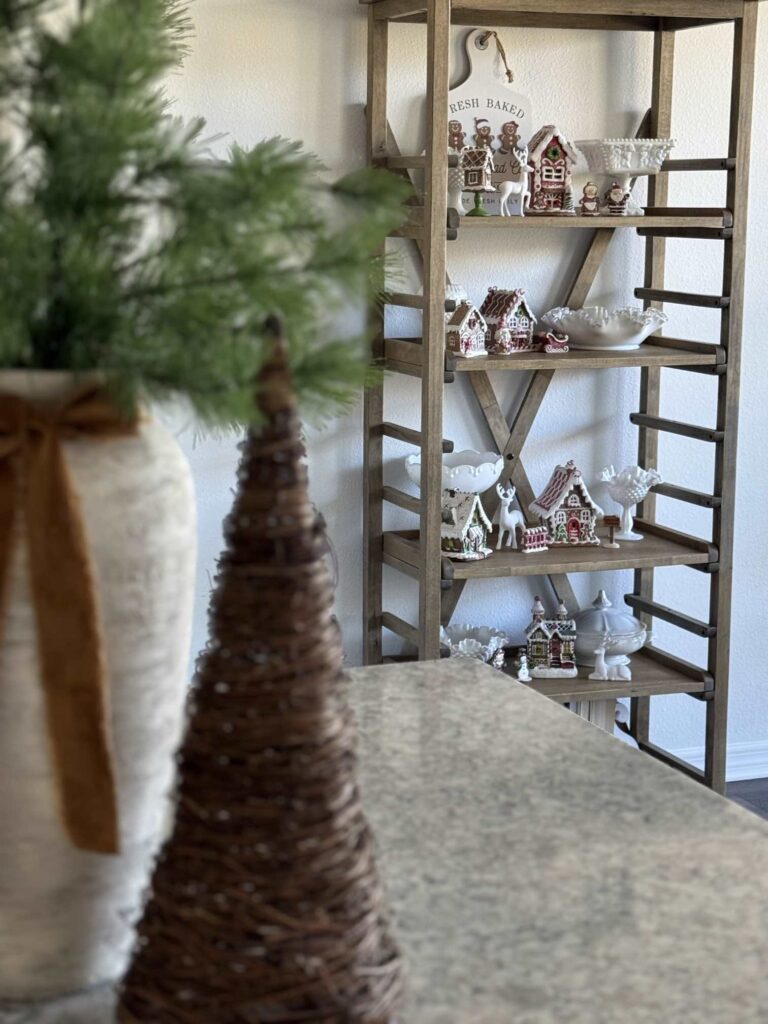 Gingerbread village Christmas decor displayed on a pie shelf. 