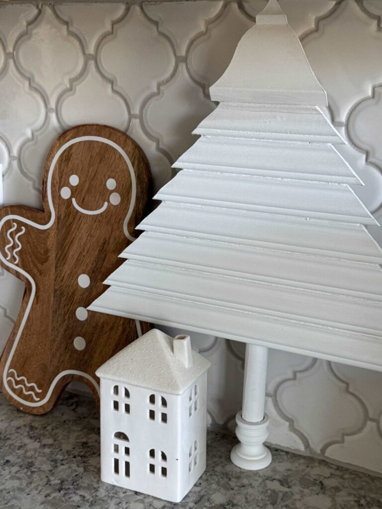 Gingerbread man Christmas decor next to a white tree and house. 