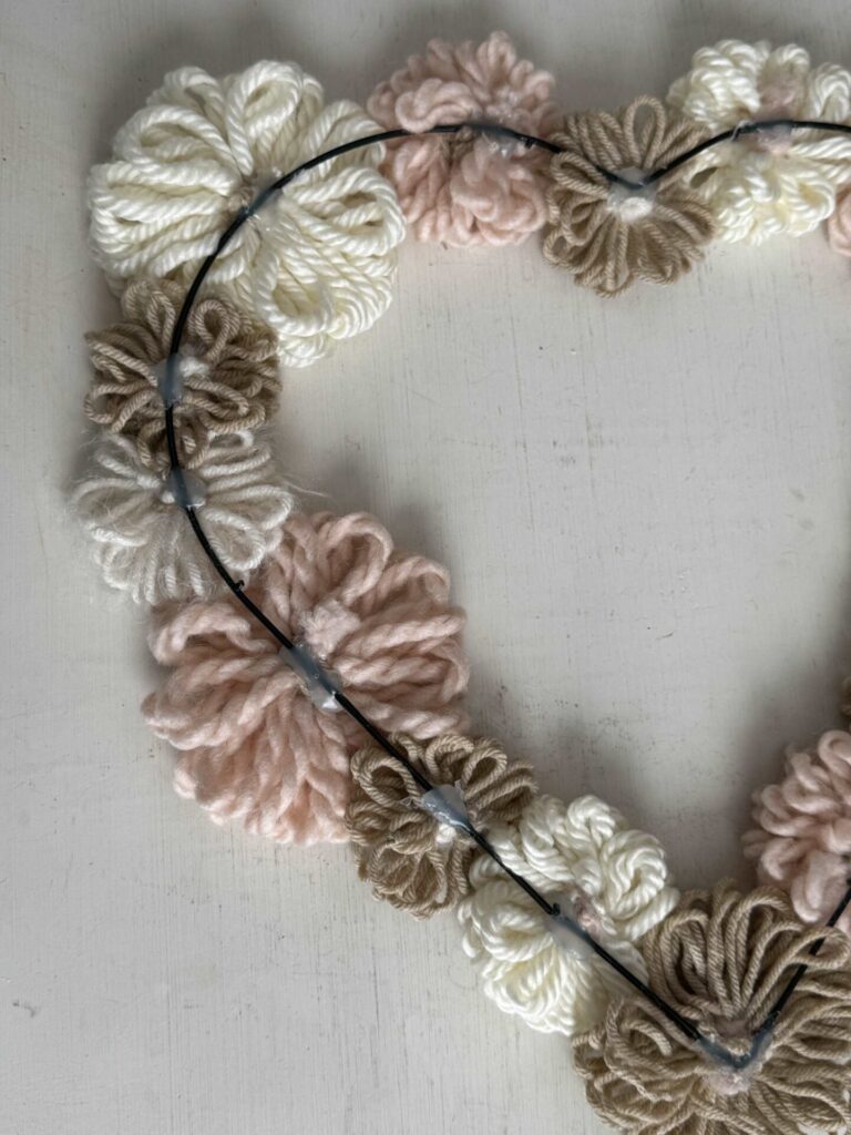 A heart shaped wire with yarn flowers glued onto it. 