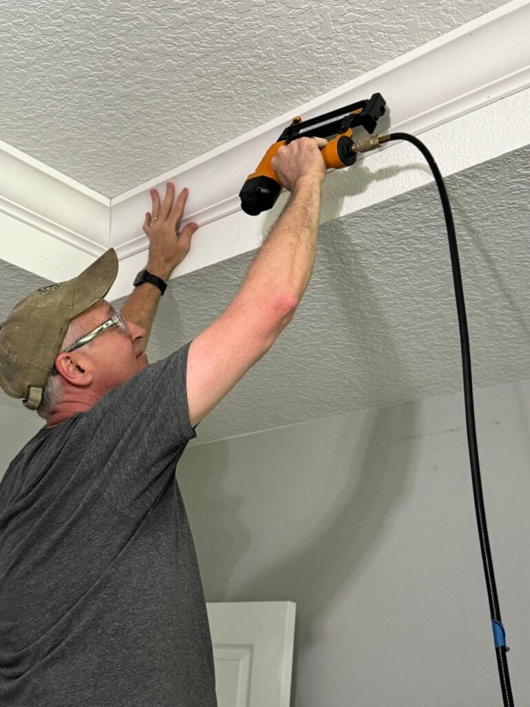 Man attaching crown molding to ceiling.