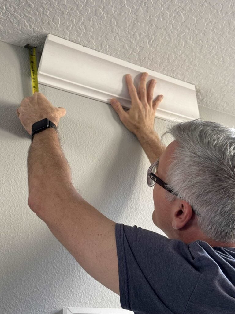 Man holding a piece of crown molding on the ceiling and measuring it.