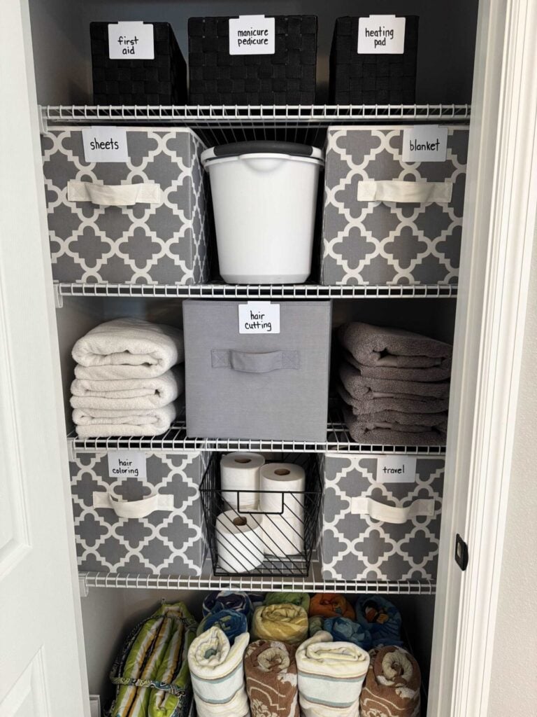 An organized bathroom closet with gray fabric bins.