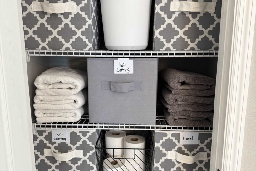 A bathroom closet organized with gray and white bins.