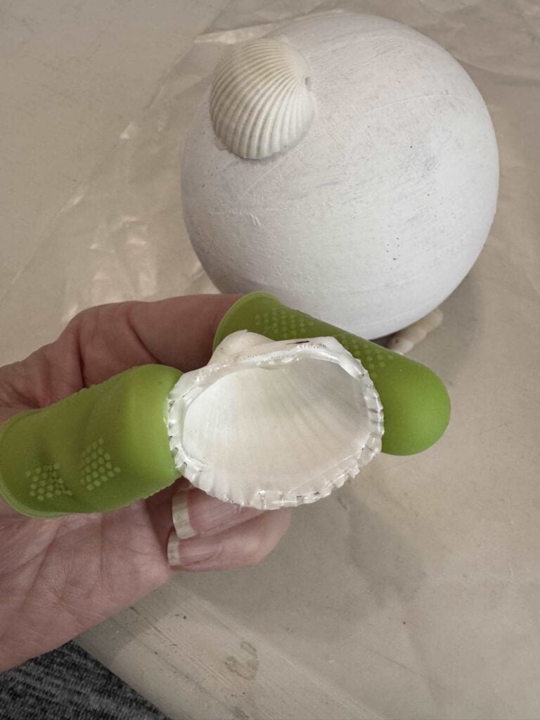 Someone wearing finder protectors and hot gluing shells onto a paper Mache ball.