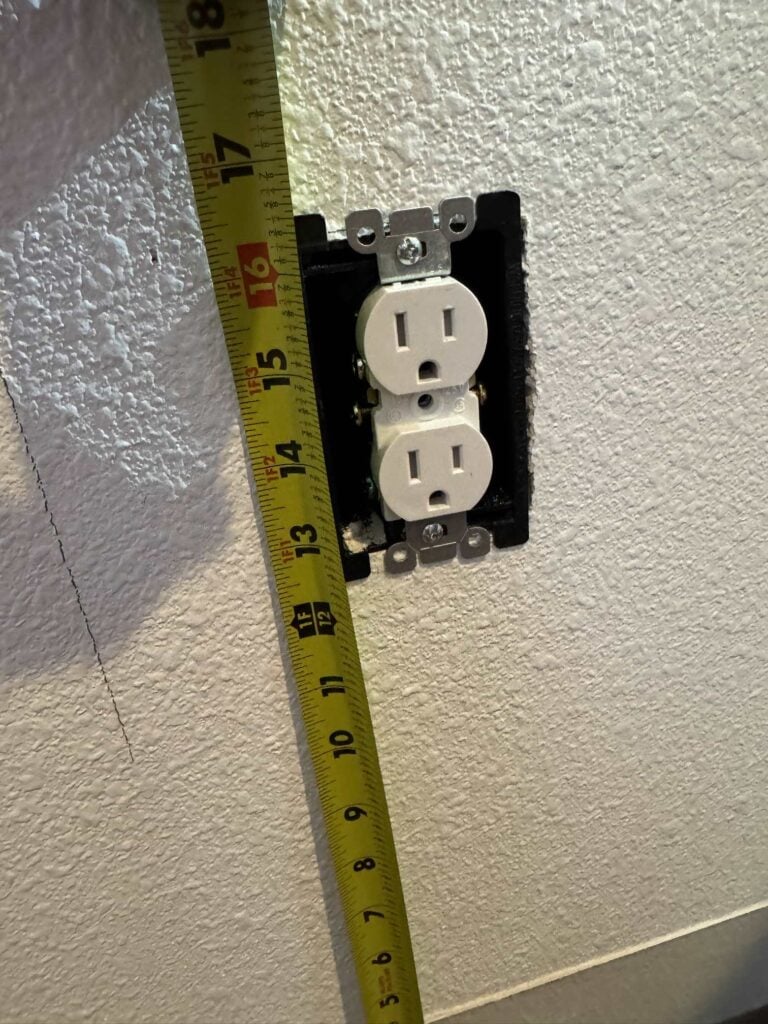 Measuring tape next to wall receptacle being used to measure how far wall outlet is from floor