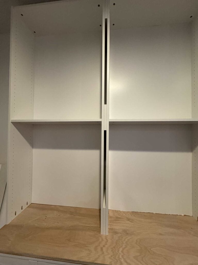 Two bookcases sitting on top of cabinets with wood scraps filling in small gap between bookcases