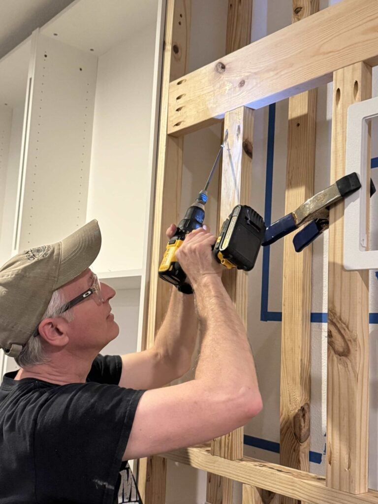 Man using drill with pocket hole extension bit to attach vertical framing board into horizontal support board with screws