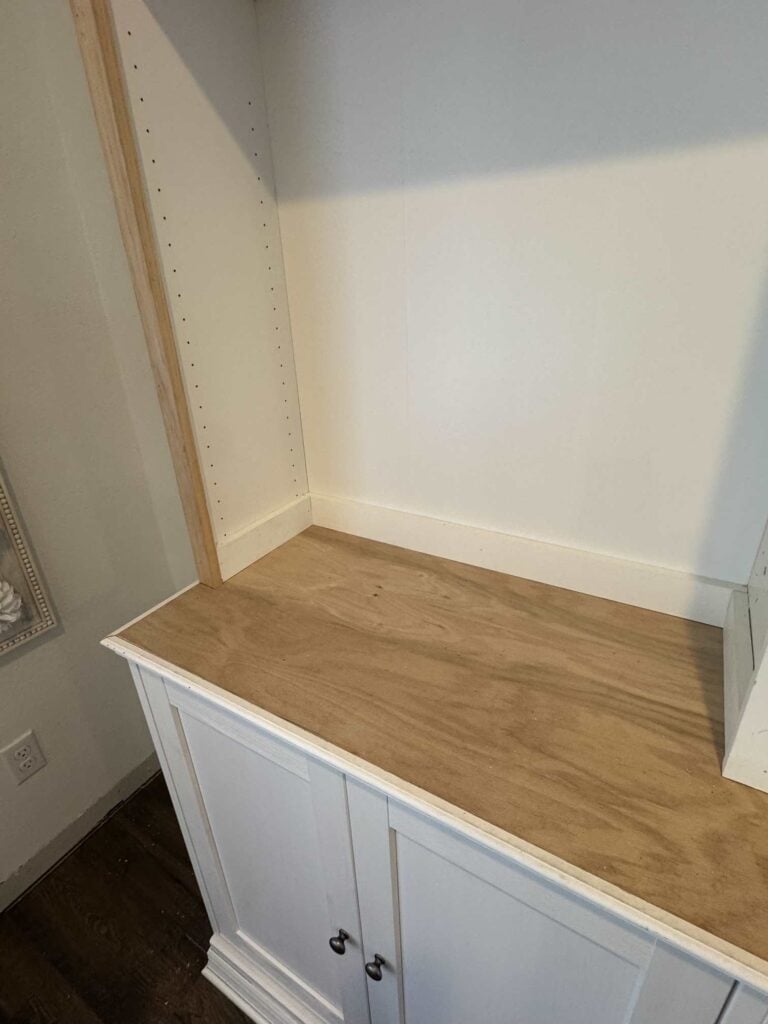 Picture partially showing white cabinet and shelves with oak countertop, white base cap, trim boards on bookshelf and baseboard trim on cabinet front