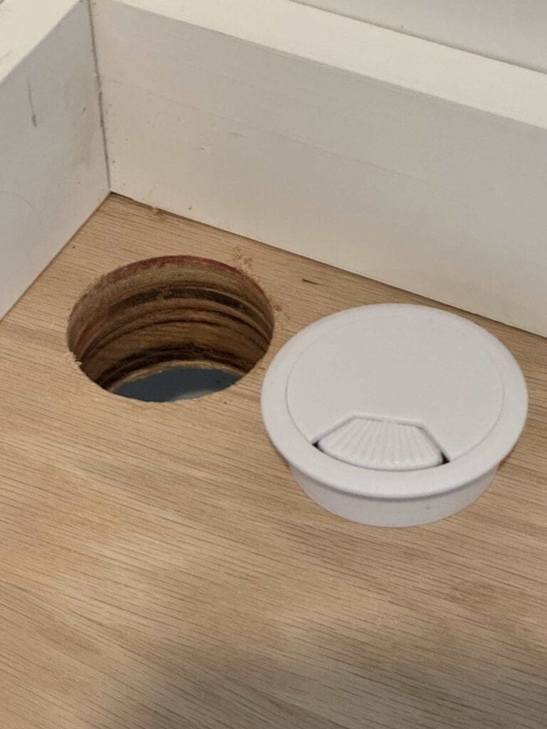 Close up picture of hole drilled in oak countertop and white desk grommet beside the hole