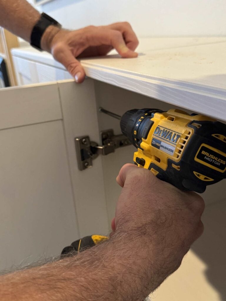 Hand holding power drill screwing in pocket screw through cabinet sidewall.