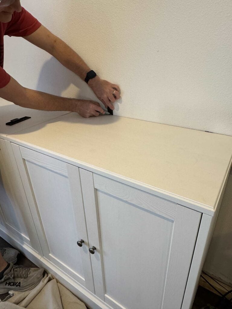 Person applying shim to gap between cabinet top and wall