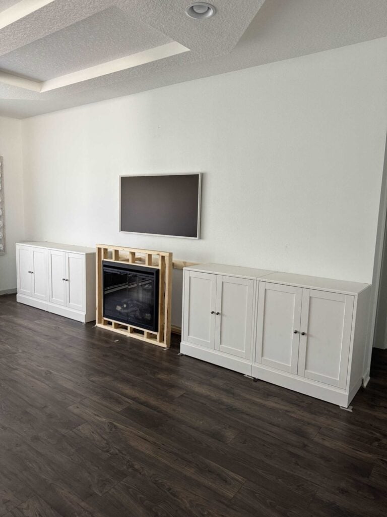 White cabinets, a fireplace insert, and a picture frame tv are the first steps of an IKEA cabinet hack for a feature wall. 