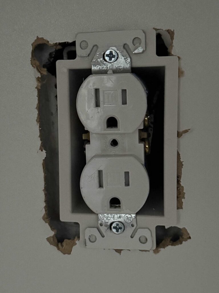 Close up picture of wall receptacle pulled through cabinet back and mounted using box extender
