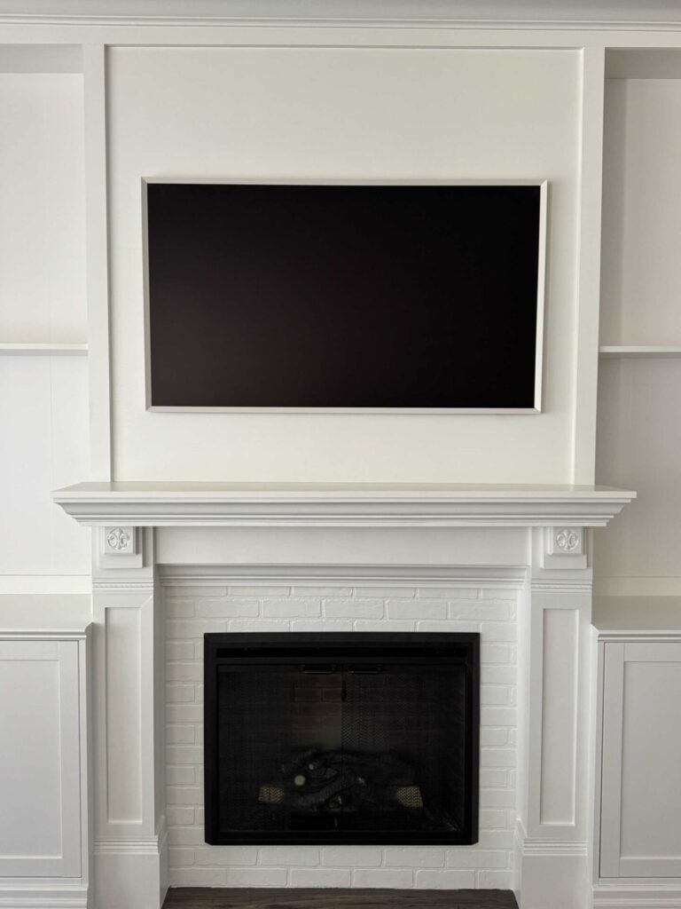 A white DIY electric fireplace and TV wall that features a frame TV and electric fireplace insert. 