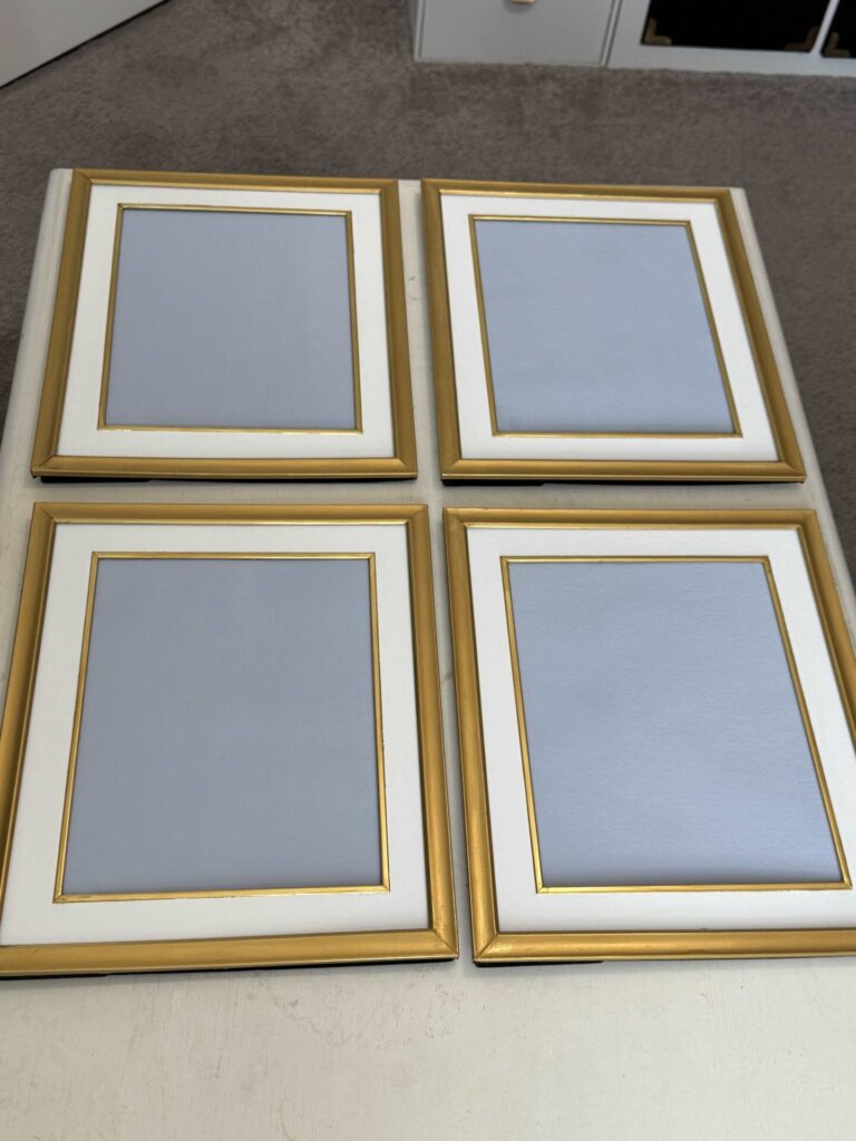 Four gold picture frames with white mats and blue center. 