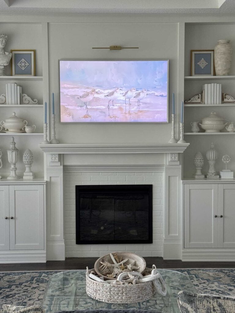 DIY electric fireplace and TV wall with art featuring shorebirds and candlesticks with blue taper candles on each end of the mantel. 