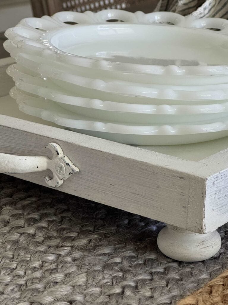 Milk glass plates stacked on a white tray with handles and feet. 