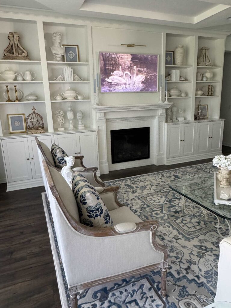 White shelves in a living room decorated with DIY framed art and white dishes and statues. 