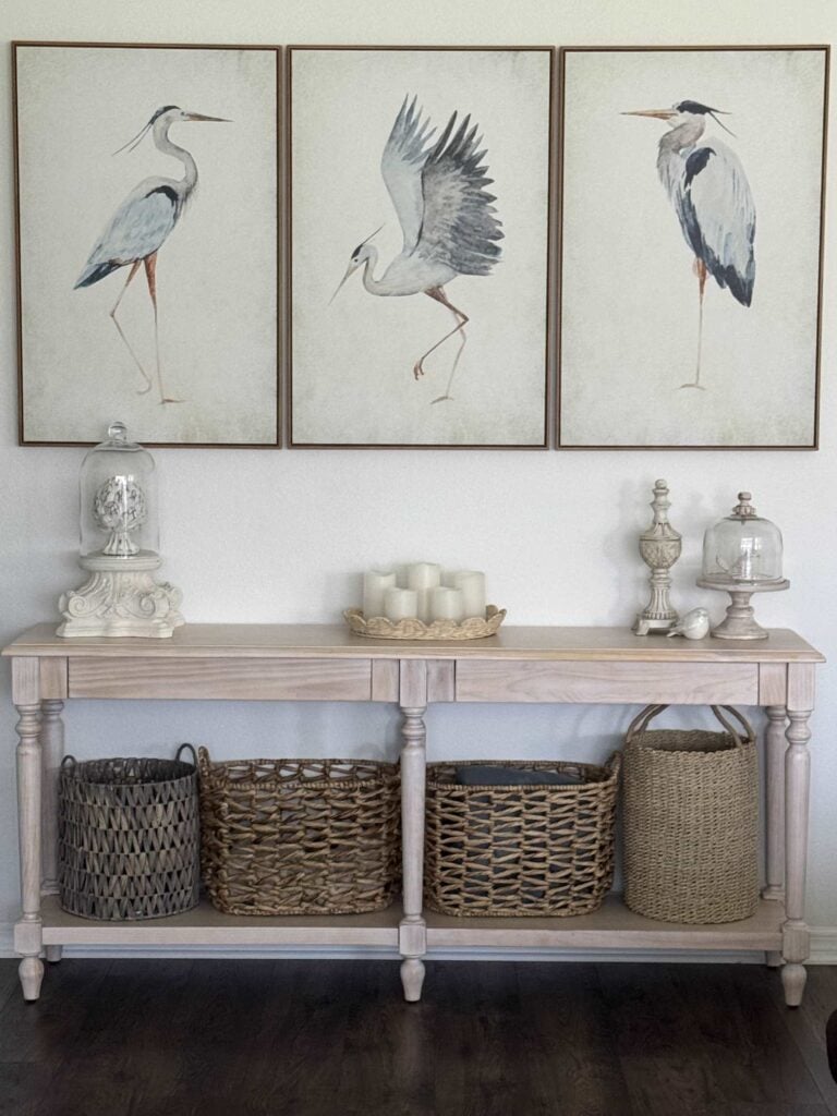 A set of three blue heron bird prints hanging over a console table. 