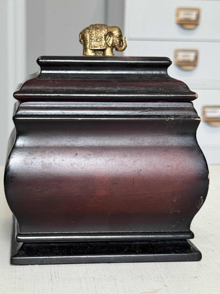 A thrift store dark decorative wood box with a gold elephant topper before a makeover.