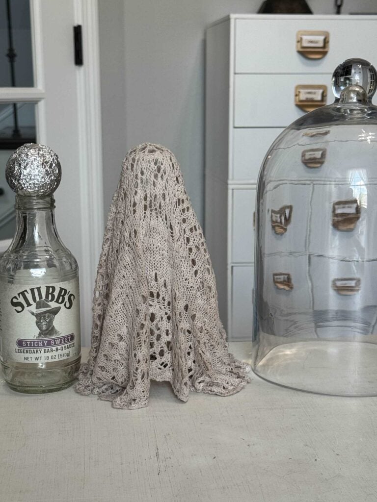Ghost made from an upcycled sweater next to a cloche and a barbecue sauce bottle with a ball wrapped in foil on it. 