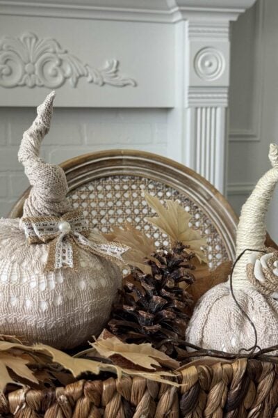 Two DIY pumpkins made from sweaters in a basket with leaves and a pinecone.