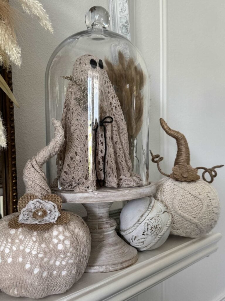 Two sweater pumpkins next to a ghost in a cloche.