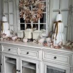 Off-white sideboard organized and decorated for fall with stacked pumpkins, leaf garlands, sweater pumpkins, and a leaf wreath.