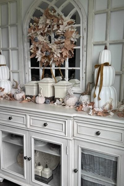 Off-white sideboard organized and decorated for fall with stacked pumpkins, leaf garlands, sweater pumpkins, and a leaf wreath.