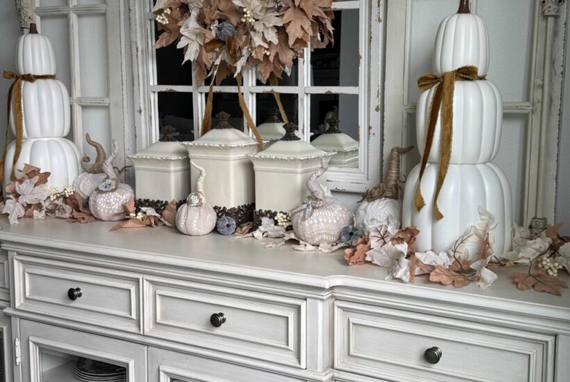 Off-white sideboard organized and decorated for fall with stacked pumpkins, leaf garlands, sweater pumpkins, and a leaf wreath.