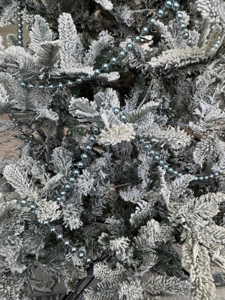 Blue bead garlands hanging in a scalloped shape on a faux flocked tree.