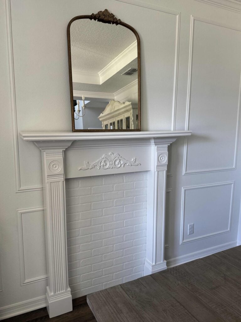 A white faux fireplace with a gold mirror sitting on the mantel.