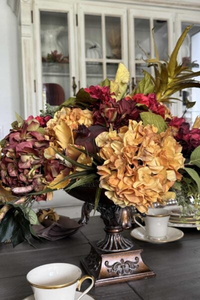 Flower arrangement in fall colors with hydrangeas, greenery, and faux fruit.