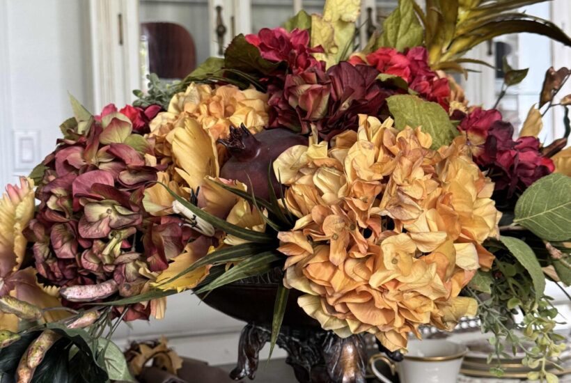 Flower arrangement in fall colors with hydrangeas, greenery, and faux fruit.