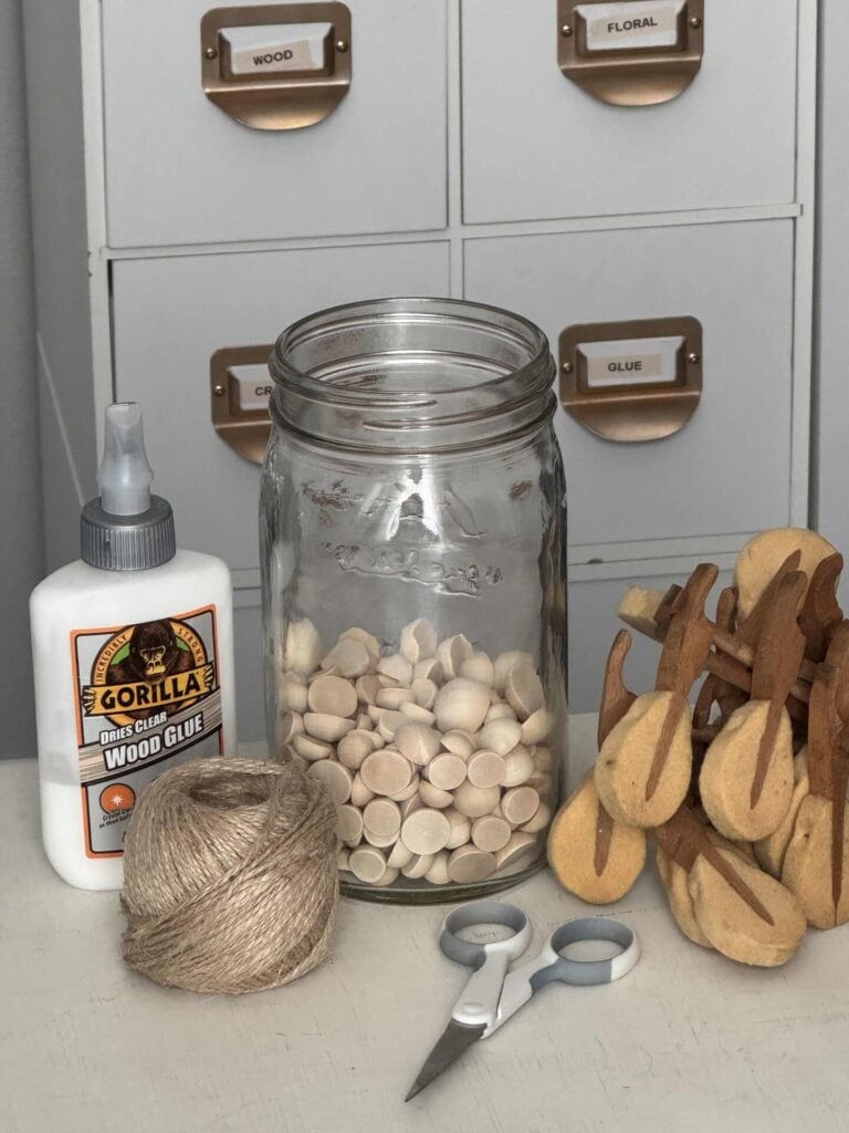 Piano hammers, jar of wood beads, wood glue, twine, and scissors used to make DIY Christmas ornaments. 