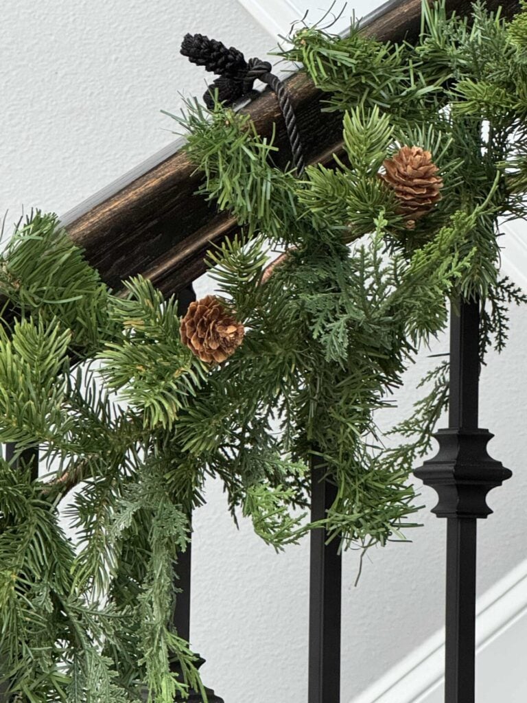 A black twist tie holding a garland onto a stair rail. 