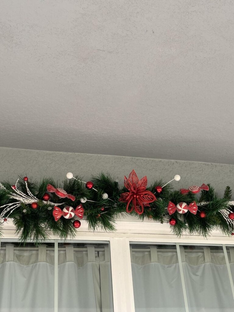 An evergreen garland decorated with red and white ornaments and a red flower in the middle. 