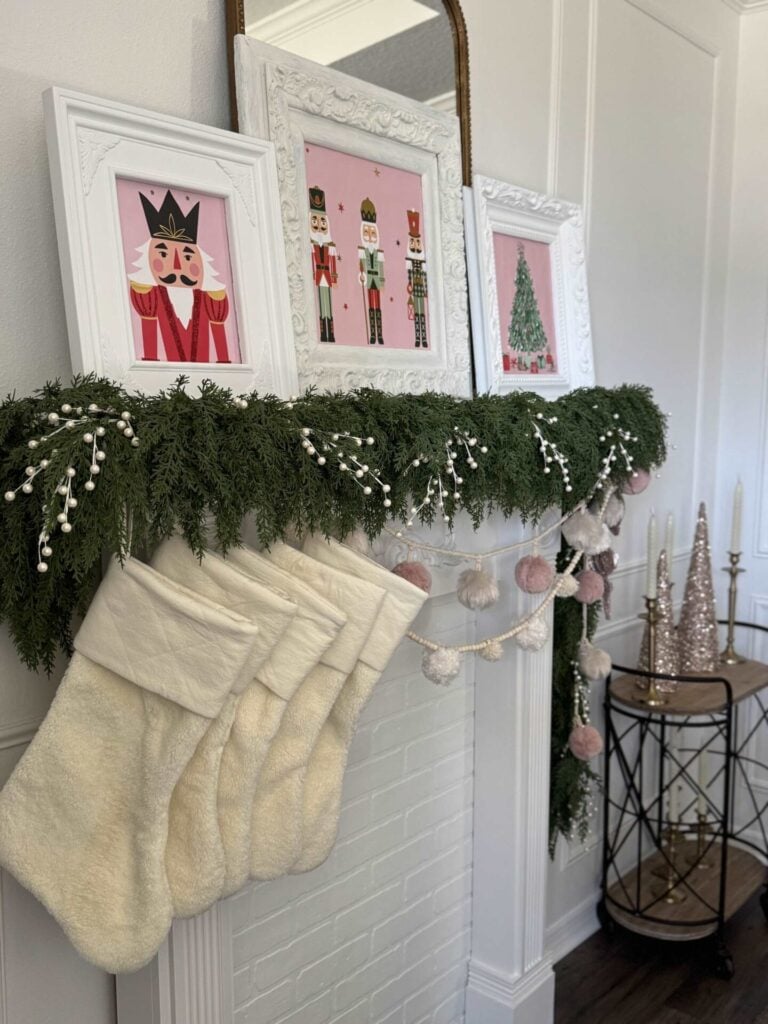 A mantel decorated for Christmas with evergreen garland, pom pom garlands, and stockings.